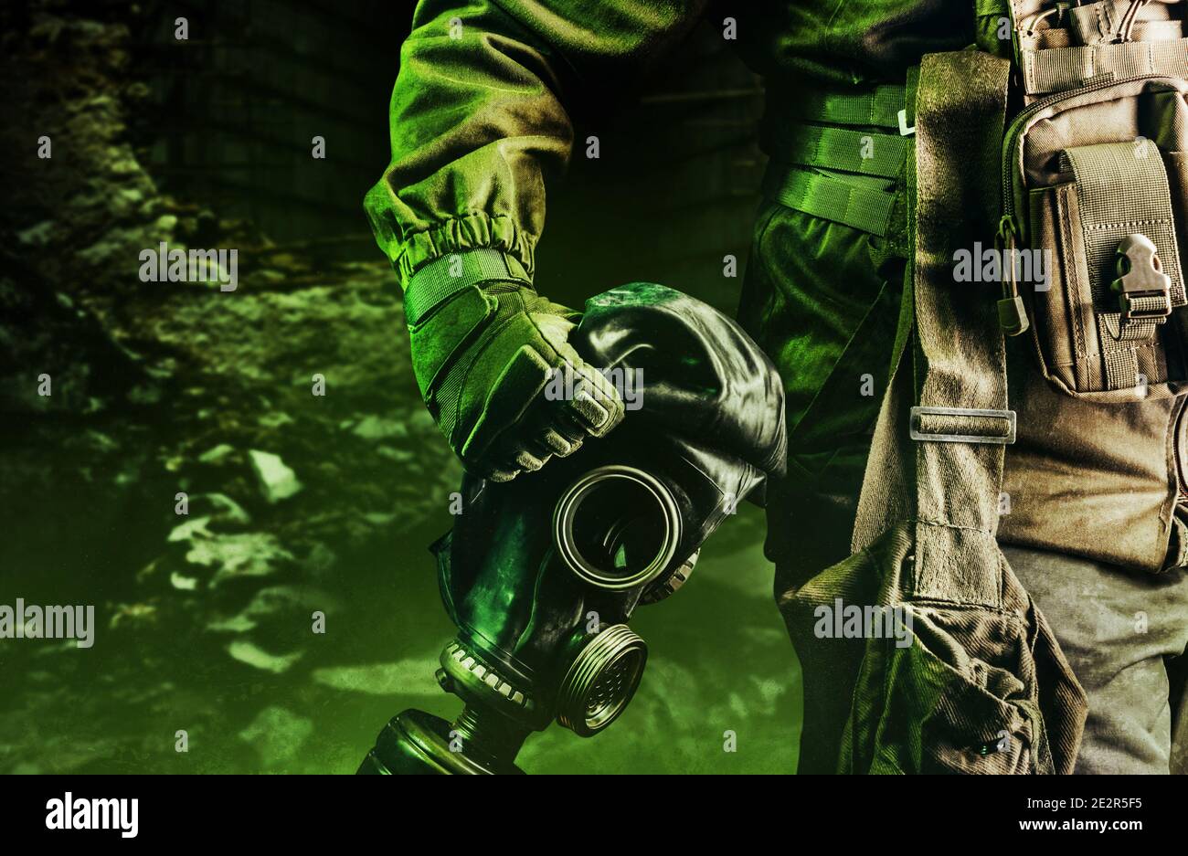 Photo d'un soldat en veste, gilet blindé et gants de protection portant un ancien masque à gaz en caoutchouc soviétique avec filtre sur fond de ruines sombres. Banque D'Images