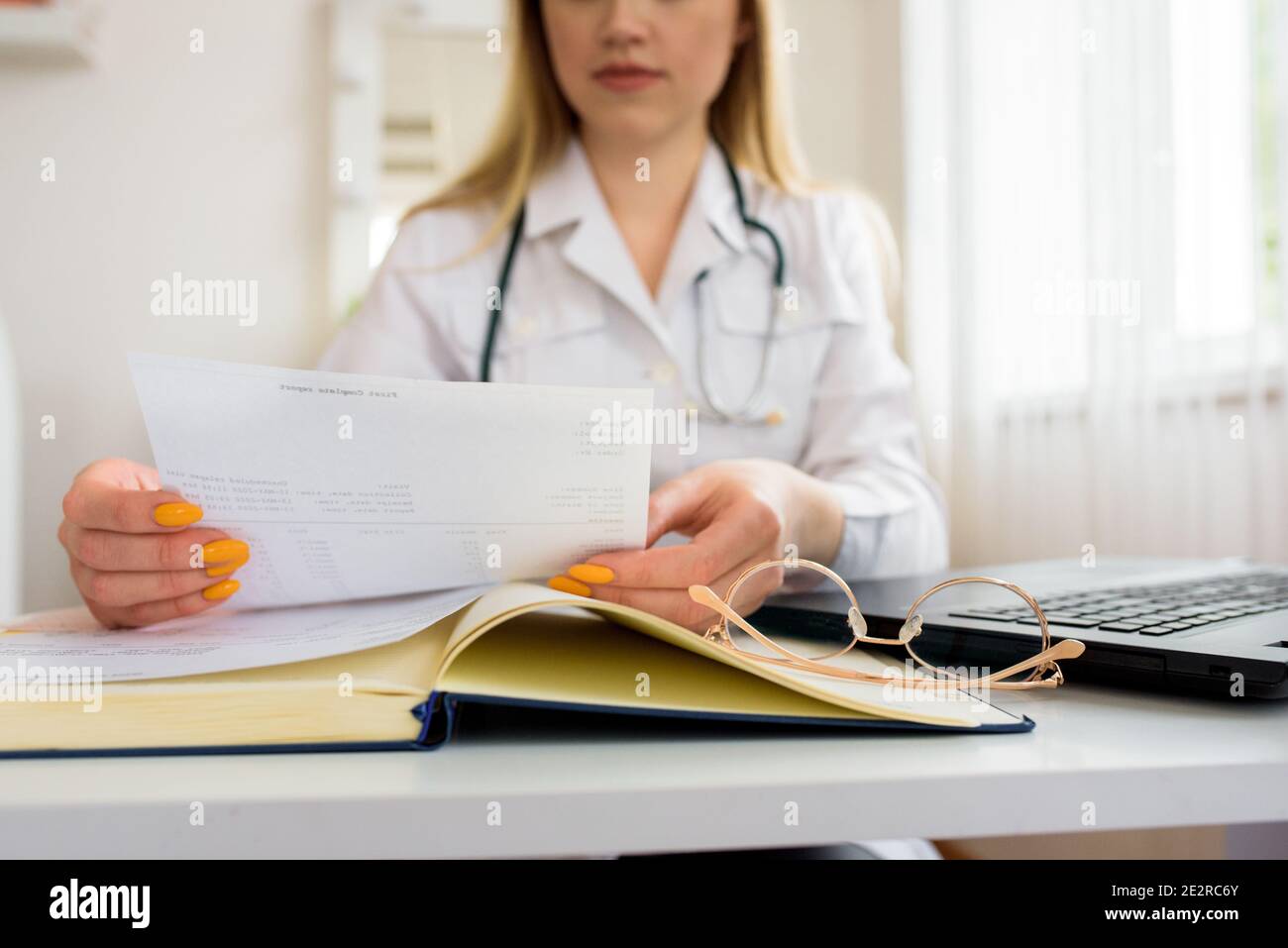 tient les comprimés rouges dans sa main. médecin dans le bureau, conseil en ligne. écrire à bloc-notes. une pile de papiers sur la table. Banque D'Images