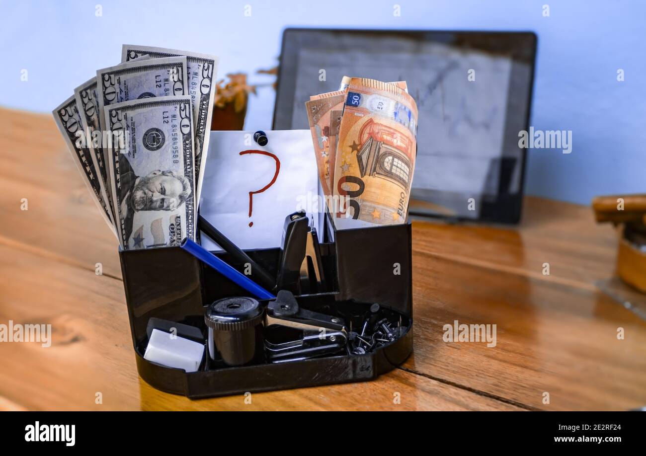 Organisateur de bureau avec deux groupes de billets, l'un en euros et l'autre en dollars, séparés par une feuille avec un point d'interrogation. Banque D'Images