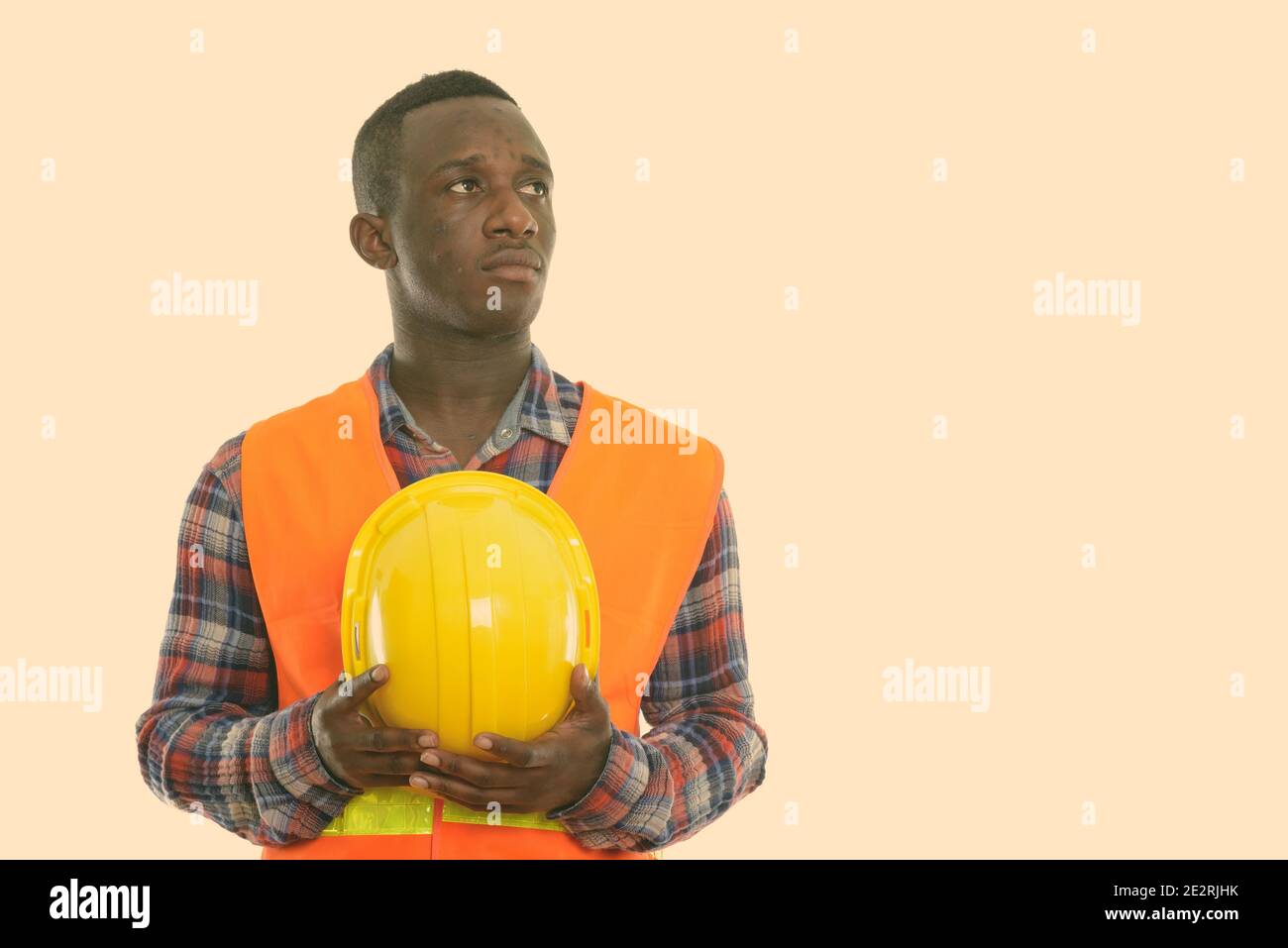 Studio shot of young black African man construction worker penser tout en regardant vers le haut et holding hard hat Banque D'Images