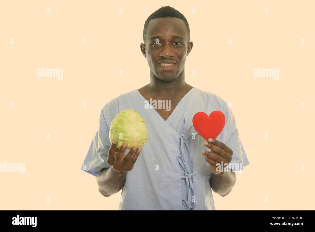Studio shot of young happy black African man smiling patient tout en maintenant le chou vert et rouge coeur Banque D'Images