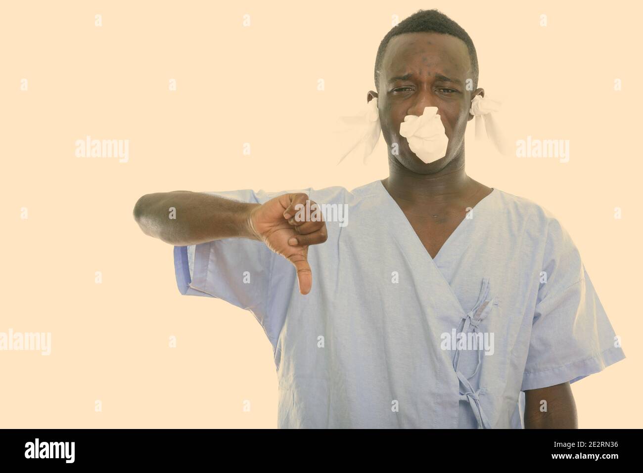 Studio shot of young black African man giving thumb patient vers le bas avec des mouchoirs dans ses oreilles et nez Banque D'Images