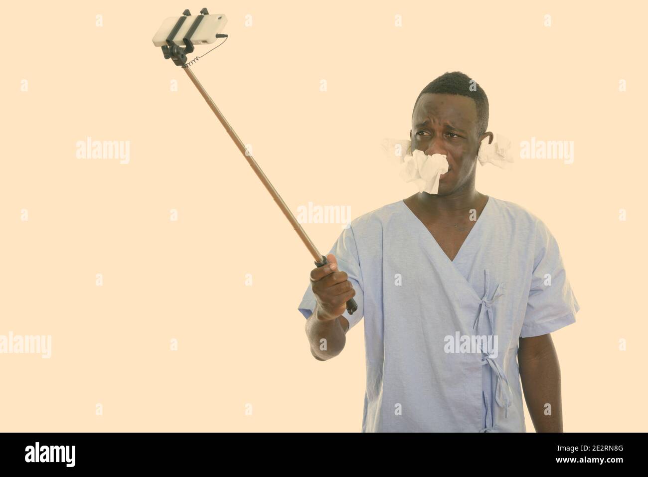 Studio shot of young black African man patient prenant photo selfies avec téléphone mobile sur les tissus avec stick selfies sur ses oreilles et nez Banque D'Images