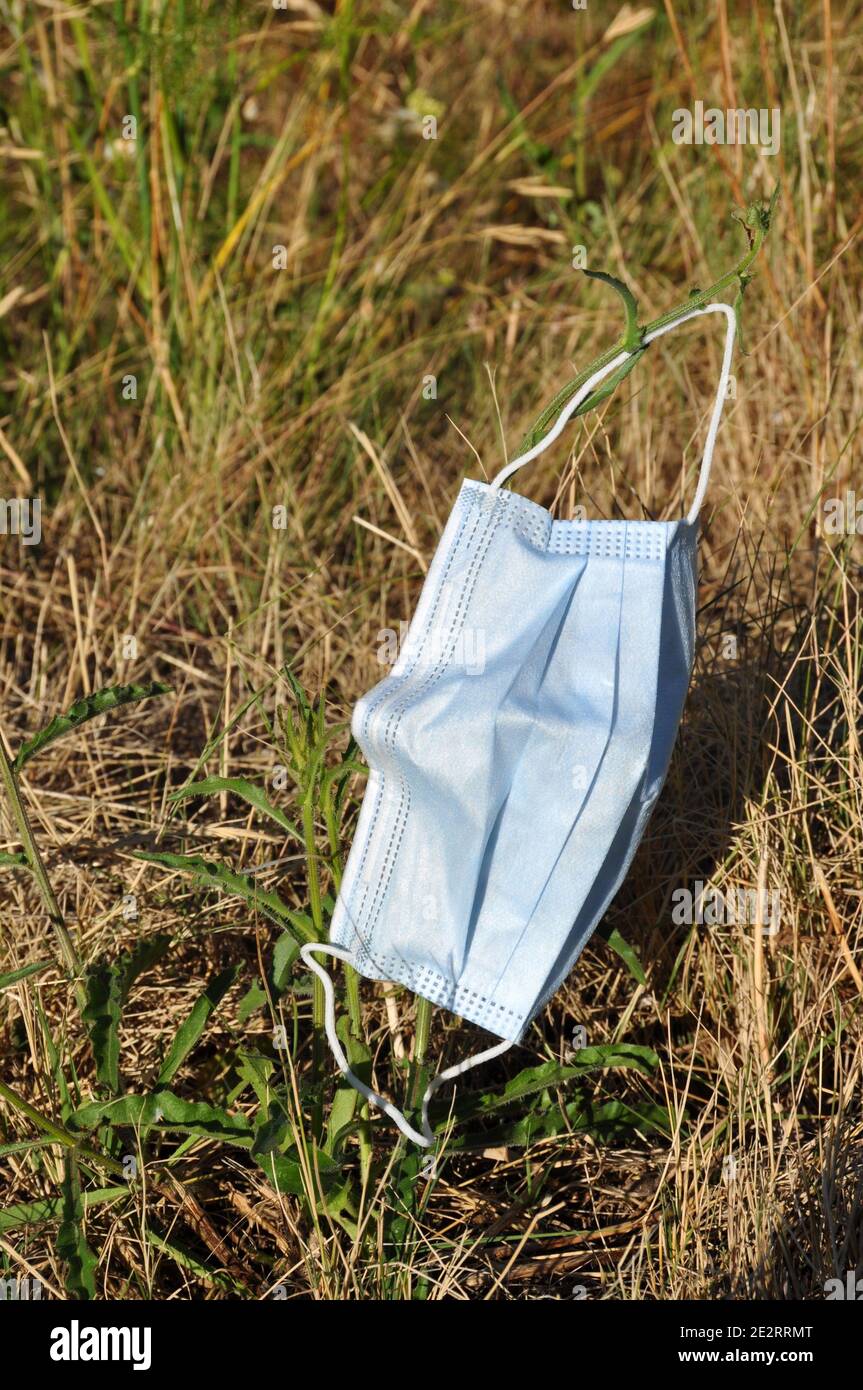 Masque jetable jeté dans un fossé à côté d'une route. Banque D'Images