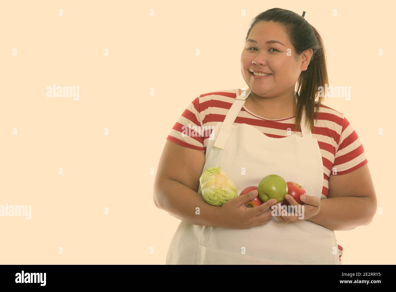 Studio shot of young woman smiling Asian fat heureux tout en maintenant les fruits et légumes avec tablier Banque D'Images