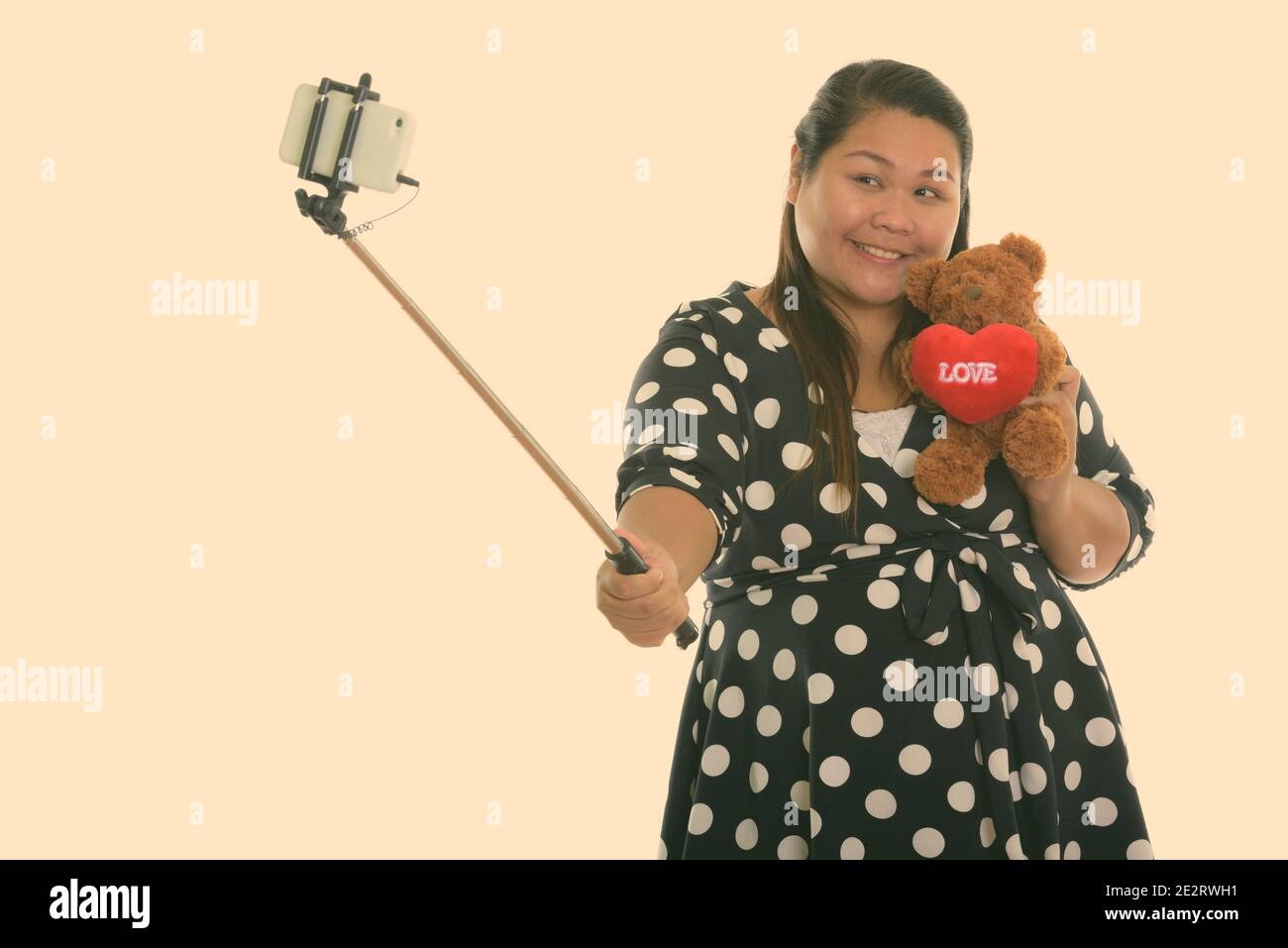 Studio de photo de jeune femme asiatique bonne graisse souriant pendant tenir l'ours en peluche avec le coeur et le signe d'amour et de prendre photo de selfie avec le téléphone mobile allumé Banque D'Images