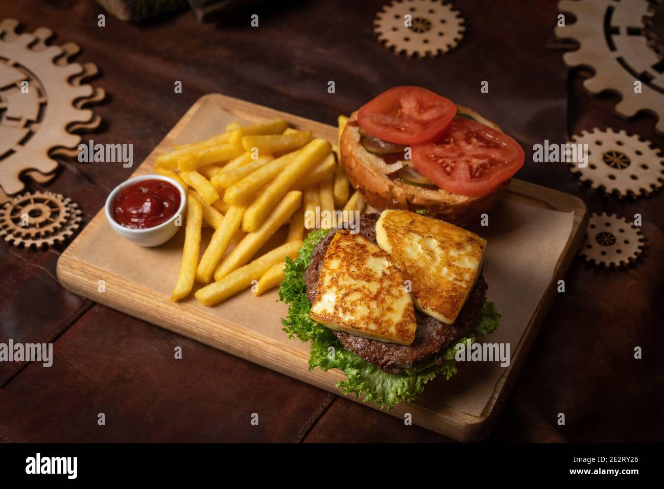 Hamburger de bœuf démonté au fromage frit, tranches de tomates servies avec des frites sur un panneau décoratif en bois avec sauce tomate et bois Banque D'Images