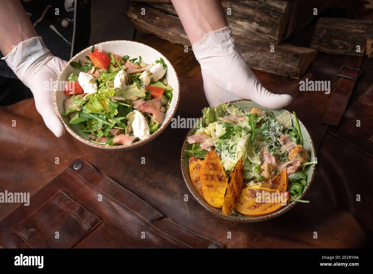 Deux bols de salade de légumes avec du saumon, de la mozzarella et des tranches de fruits grillées se dressent sur une table recouverte d'un chiffon en cuir. Restaurant Banque D'Images