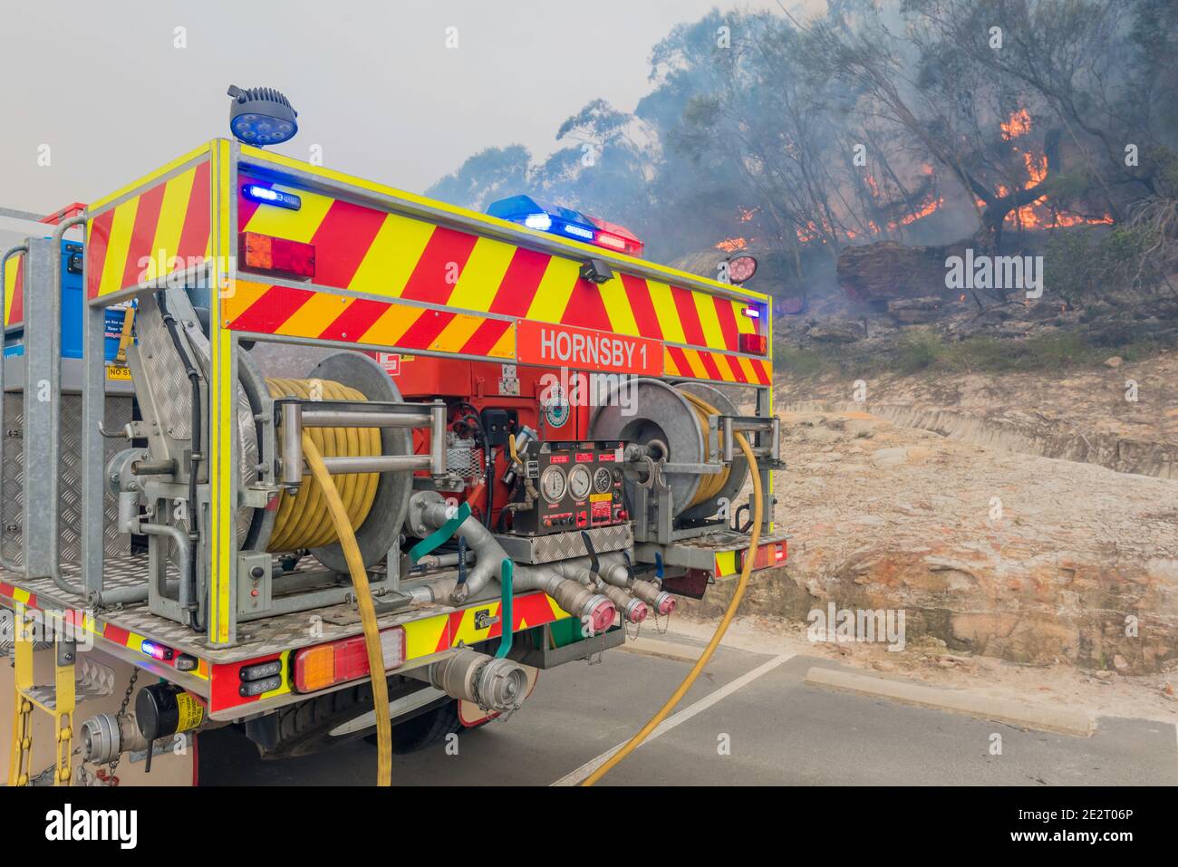 L'arrière d'un camion de service d'incendie rural avec des feux clignotants et un feu en arrière-plan lors d'une combustion de réduction des risques à Sydney, en Australie Banque D'Images