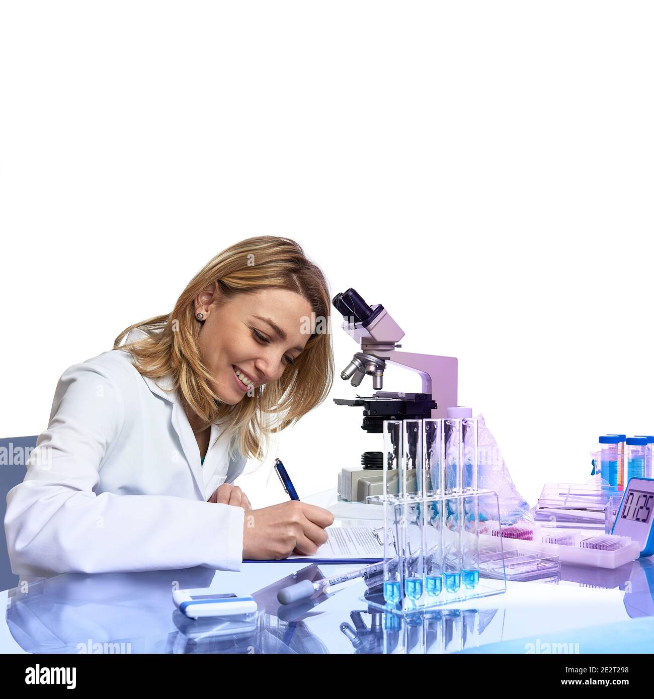 Une jeune femme scientifique ou technique écrit un rapport ou un journal de laboratoire dans un laboratoire moderne avec microscope, tubes en verre avec des échantillons dans des tubes, cette image est Banque D'Images