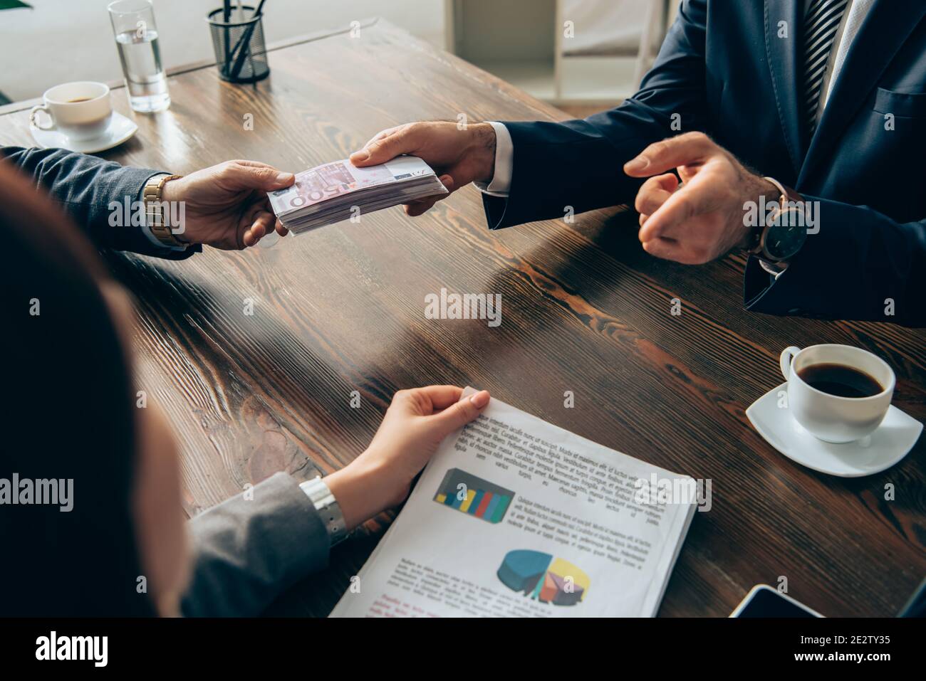 Investisseur donnant de l'argent à l'homme d'affaires et pointant vers femme d'affaires avec papiers sur un premier plan flou Banque D'Images
