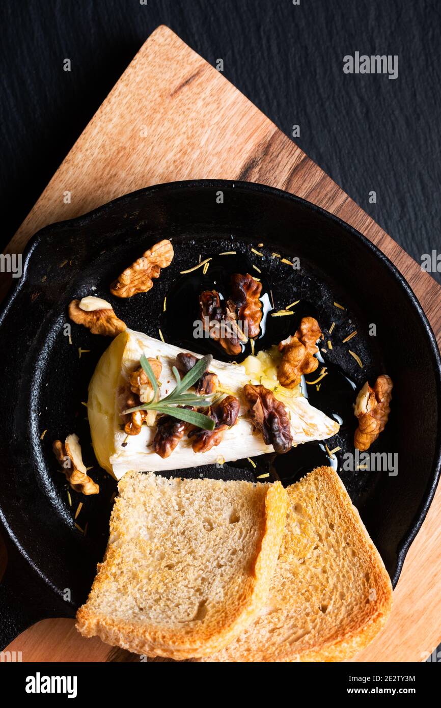 Concept de la nourriture point focus fromage de Brie cuit maison avec du miel et noix dans poêle à frire fer sur planche de bois avec espace de copie en pierre d'ardoise noire Banque D'Images