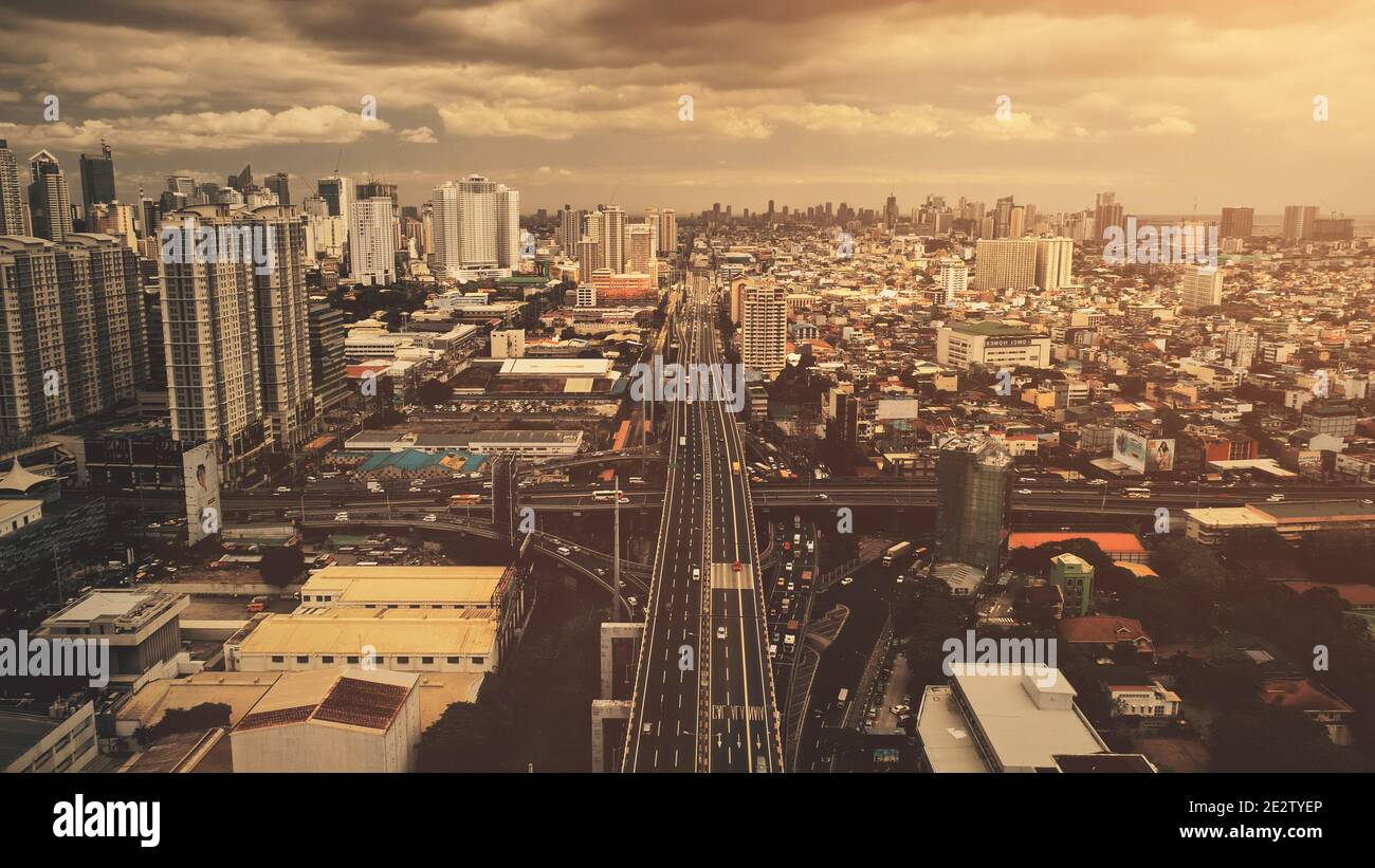 Traversez le pont routier à l'antenne du coucher du soleil. Gratte-ciels modernes dans la rue du centre-ville. Paysage urbain de Manille à la lumière du soleil. Paysage urbain cinématographique de la capitale des Philippines au tir de drone Banque D'Images