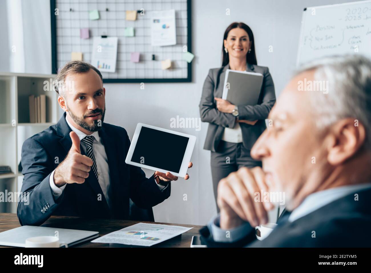 Homme d'affaires avec une tablette numérique montrant comme un collègue souriant et investisseur sur un premier plan flou Banque D'Images
