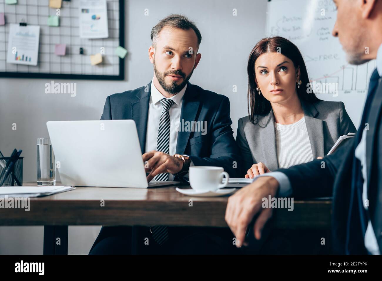 Les hommes d'affaires avec un ordinateur portable qui regarde un investisseur mature sur un premier plan flou au bureau Banque D'Images