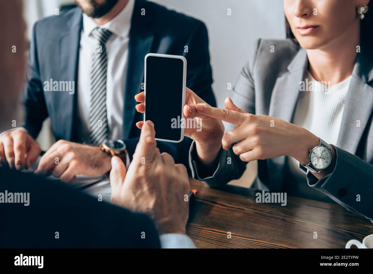 Vue rognée d'une femme d'affaires pointant vers un smartphone avec un écran vide proche collègue et investisseur sur un premier plan flou Banque D'Images