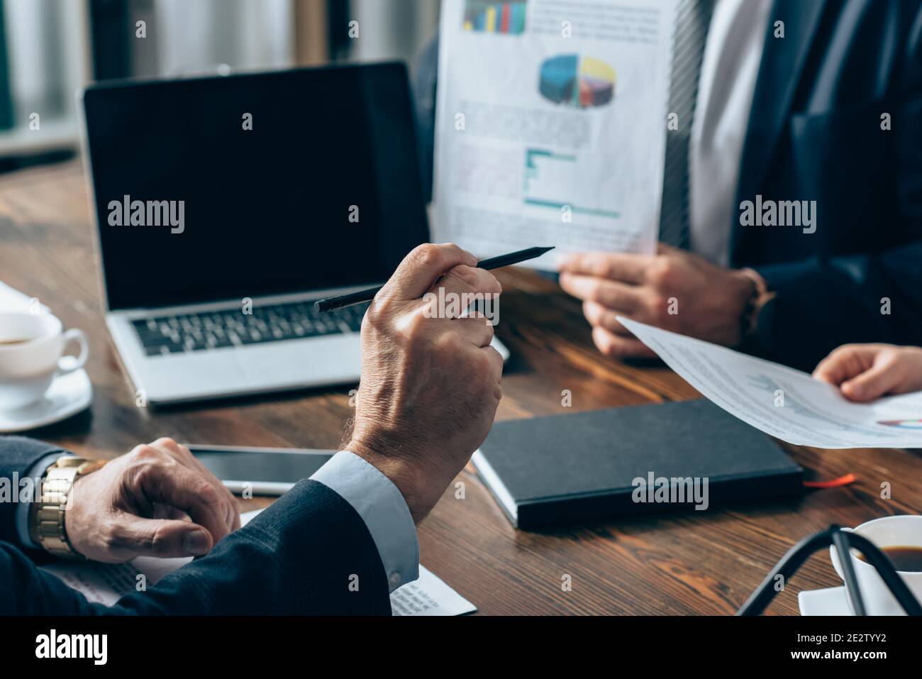 Vue rognée de l'investisseur pointant vers des professionnels avec des documents près des périphériques sur un arrière-plan flou Banque D'Images
