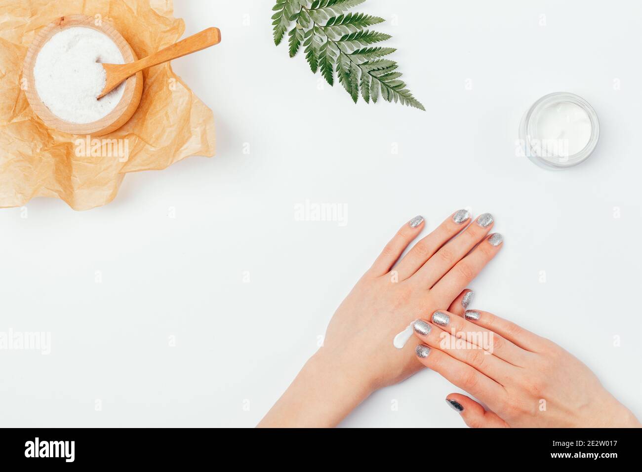 Soin de la peau des mains, gommage naturel au sel de mer à côté des mains  des femmes appliquant de la crème nourrissante, vue de dessus sur la table  blanche Photo Stock -