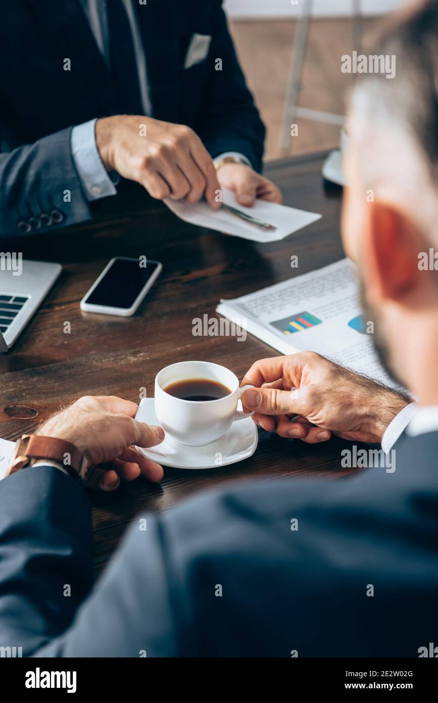 Tasse de café entre les mains de l'homme d'affaires proche investisseur avec enveloppe et papier sur fond flou Banque D'Images