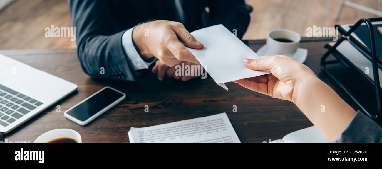 Vue rognée d'une femme d'affaires qui prend l'enveloppe de l'investisseur près du café et des appareils sur une table, une bannière Banque D'Images