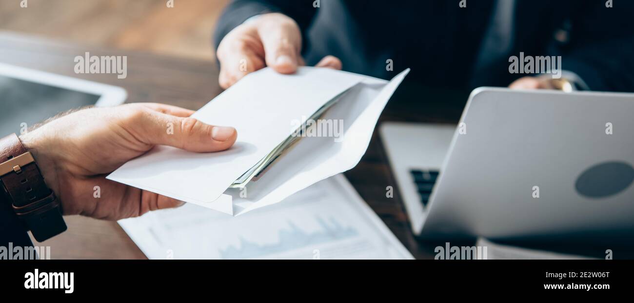 Vue rognée de l'homme d'affaires prenant enveloppe avec l'argent de l'investisseur près de l'ordinateur portable sur un arrière-plan flou, bannière Banque D'Images