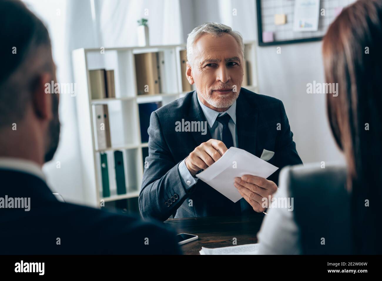 Investisseur mature tenant une enveloppe près des gens d'affaires sur un premier plan flou au bureau Banque D'Images