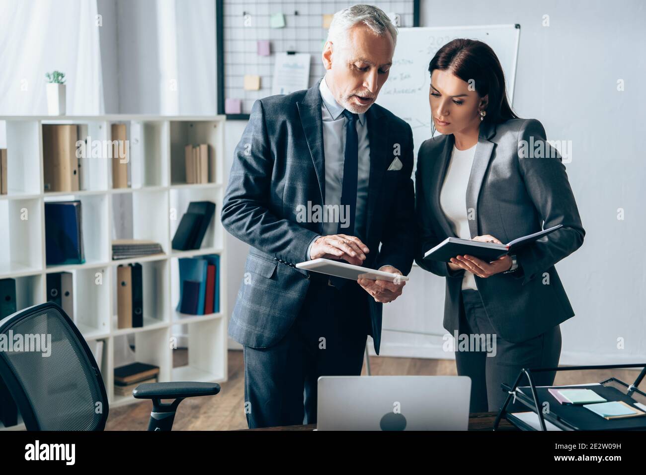 Investisseur utilisant une tablette numérique près d'une femme d'affaires avec un ordinateur portable pendant le conseil Banque D'Images