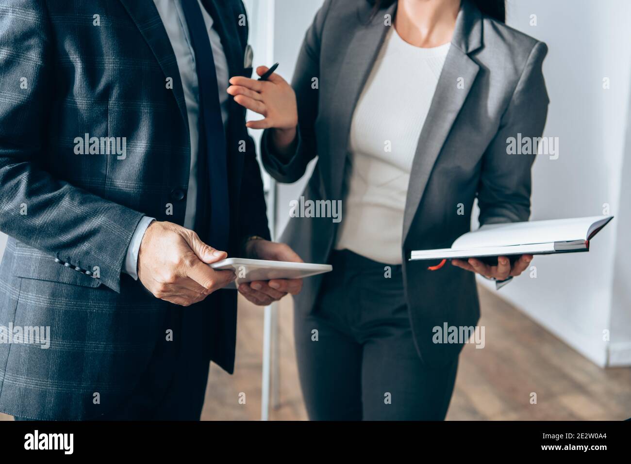 Vue rognée d'une femme d'affaires avec bloc-notes et stylo pointant vers investisseur avec une tablette numérique Banque D'Images