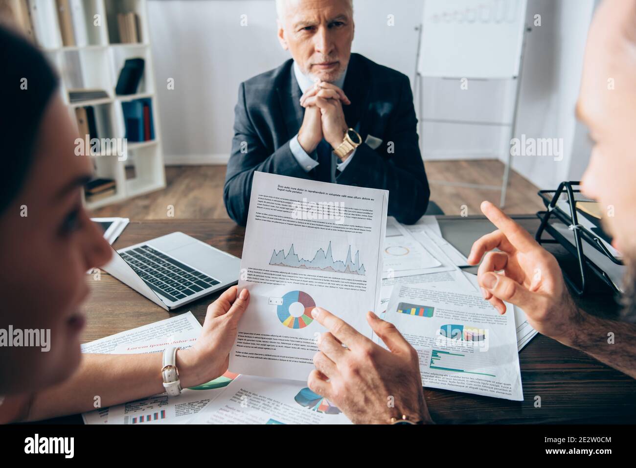 Homme d'affaires pointant du doigt sur un document avec des graphiques près d'un collègue et investisseur sur fond flou pendant la consultation Banque D'Images