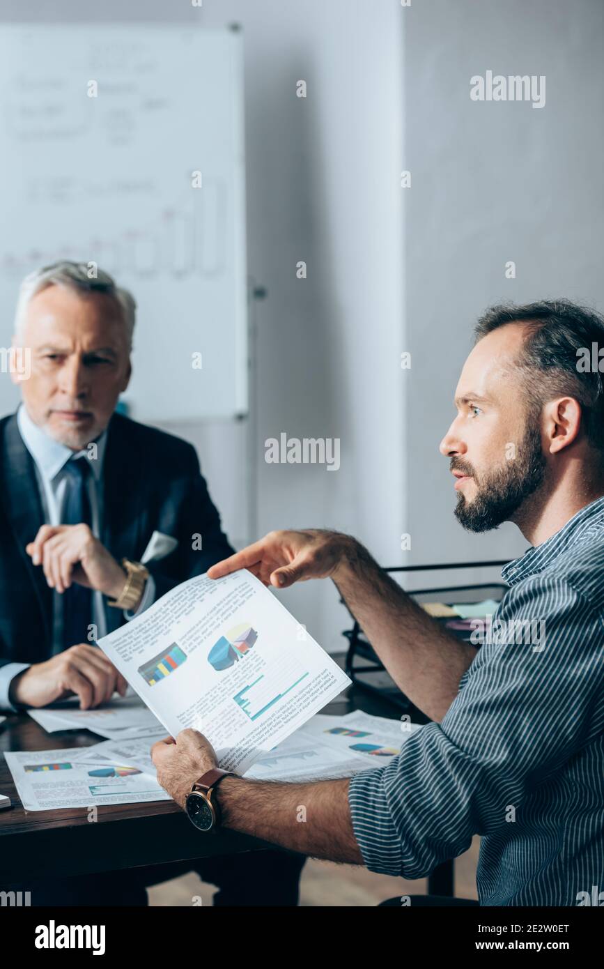 Homme d'affaires tenant le papier avec des graphiques près de l'investisseur sur un fond flou au bureau Banque D'Images