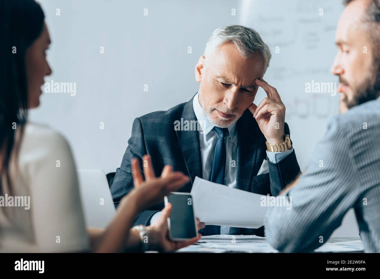 Investisseur mature qui regarde des documents alors que les professionnels ont un smartphone parler au premier plan flou Banque D'Images