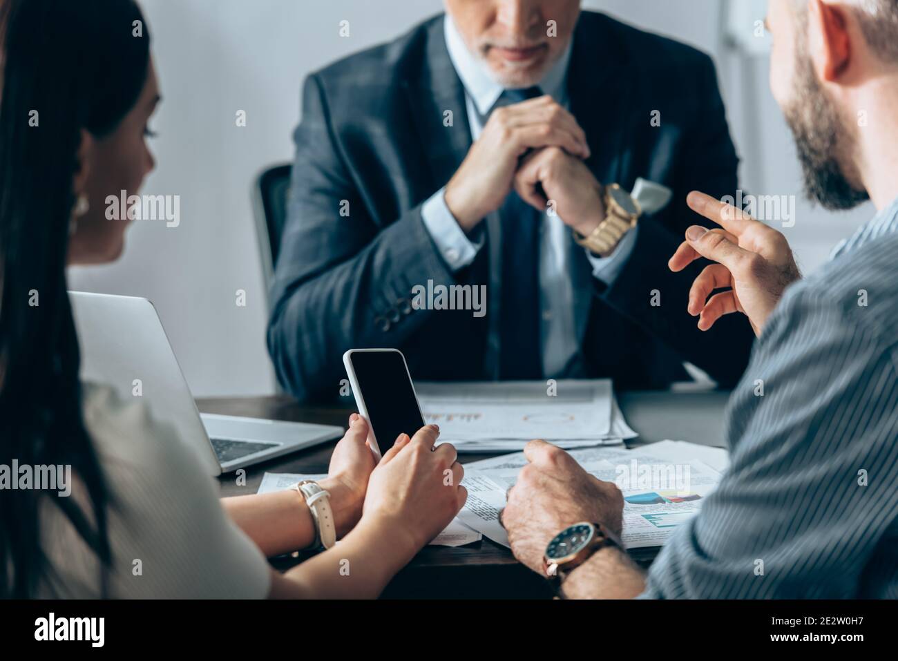 Homme d'affaires pointant du doigt près d'un collègue avec un smartphone et un investisseur sur un arrière-plan flou au bureau Banque D'Images