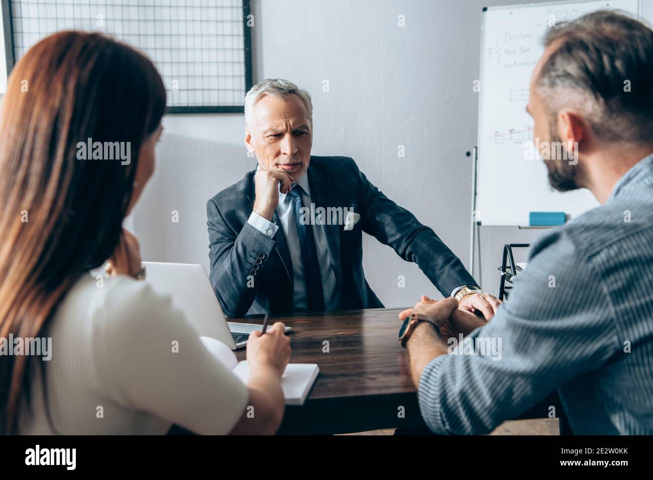 Investisseur pensif regardant les partenaires d'affaires sur un premier plan flou près ordinateur portable et portable sur table Banque D'Images
