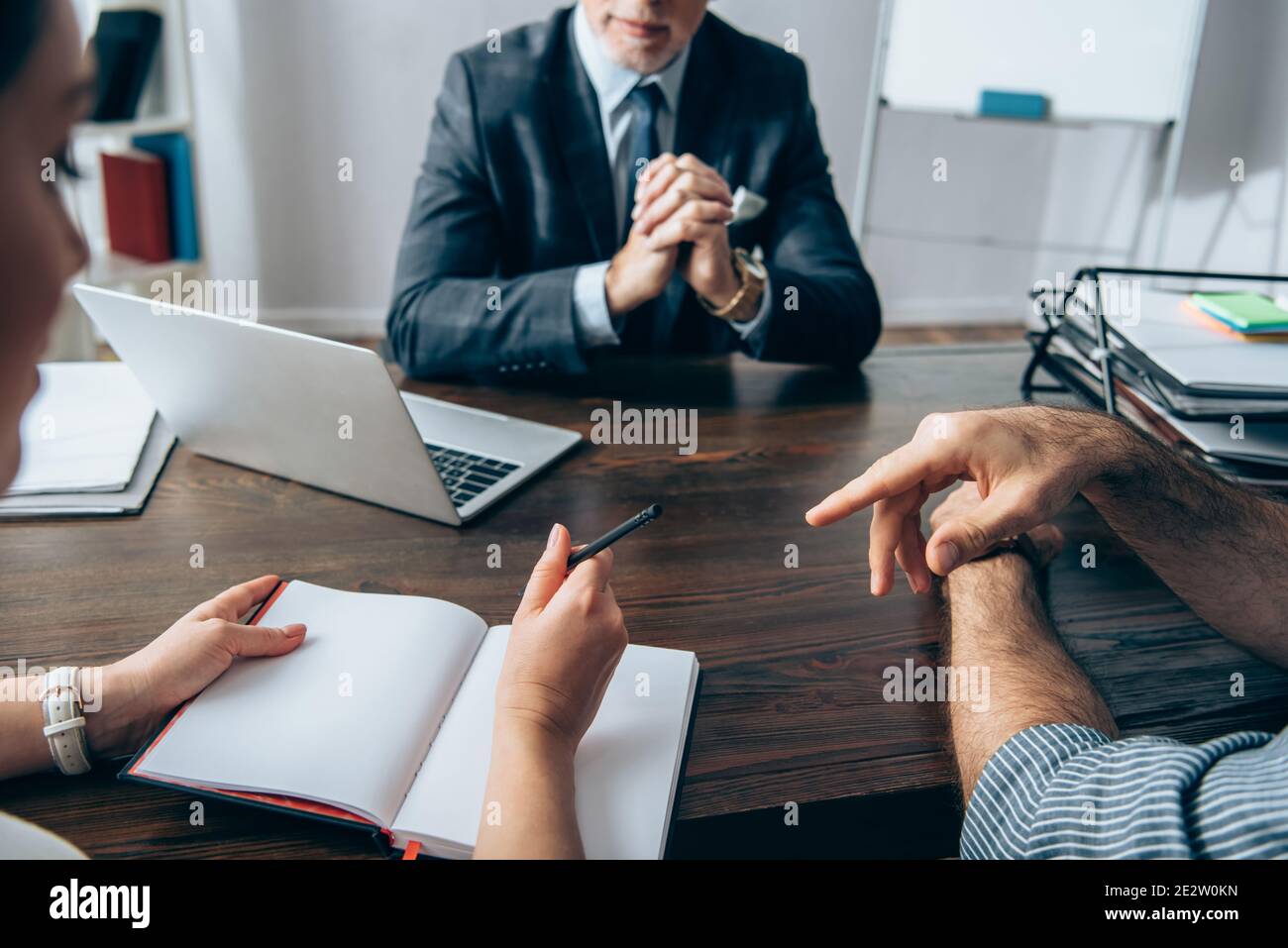 Homme d'affaires pointant du doigt près d'un collègue avec un stylo, un ordinateur portable et un investisseur sur un arrière-plan flou au bureau Banque D'Images