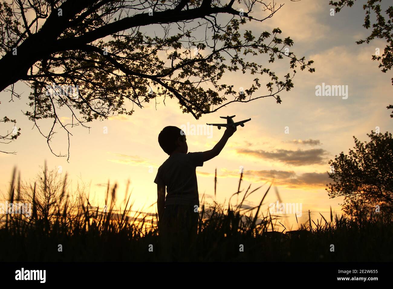 Un petit garçon en silhouette tenant un avion dans le champ à un magnifique coucher de soleil symbolisant la paix dans le monde Banque D'Images