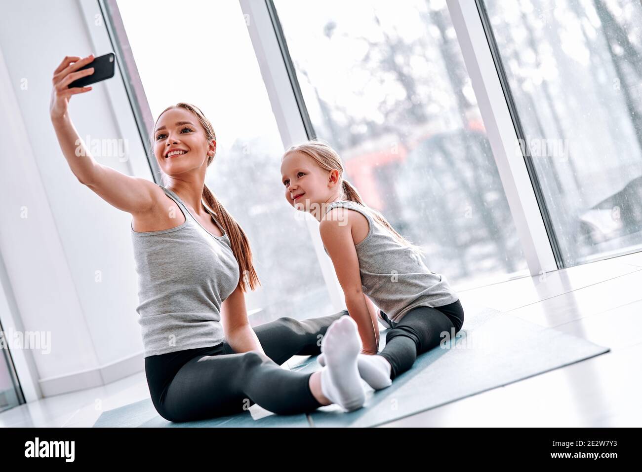 Jeune maman sport blogueur faisant selfie avec sa petite fille mignonne tout en faisant l'échauffement, exercices d'étirement en cours de yoga. Concept de blog de sport familial Banque D'Images