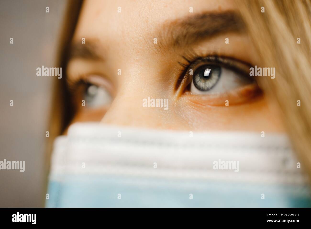 Vue macro: Belle jeune femme avec des yeux bleus portant un masque médical et regardant loin Banque D'Images