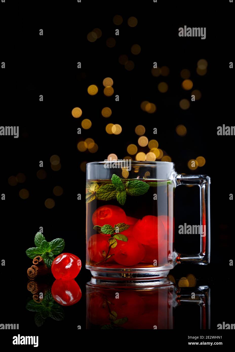 Thé chaud à la cerise avec cannelle et menthe dans une tasse en verre sur table miroir et arrière-plan noir Banque D'Images