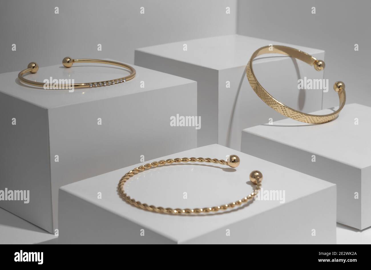 Trois bracelets dorés modernes sur fond géométrique blanc Banque D'Images