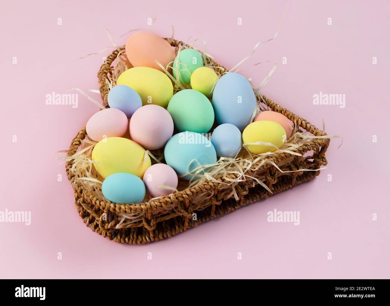 Oeufs de Pâques multicolores pastel dans un panier en forme de coeur sur fond rose. Vue de dessus, placer pour le texte. Carte de vœux. Banque D'Images