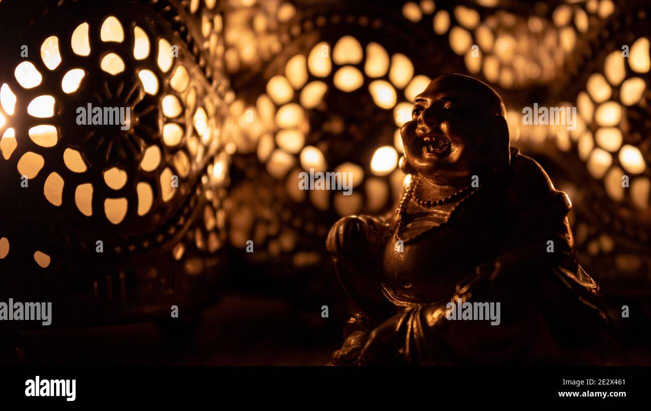 Figurine Golden Laughing Buddha avec bougies ornées créant des ombres chaudes dans une ambiance sombre Banque D'Images