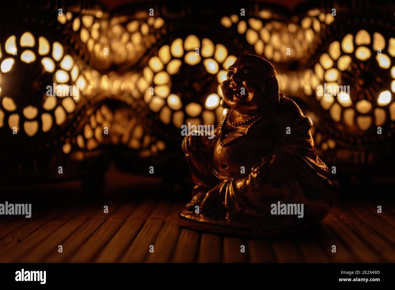 Figurine Golden Laughing Buddha avec des bougies complexes créant des ombres chaudes et méditatives Banque D'Images