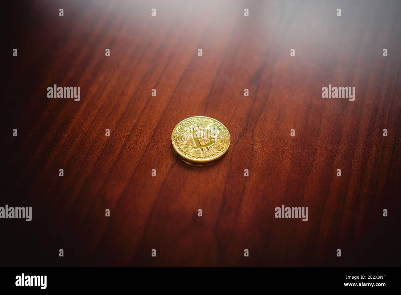 Un bitcoin d'or solitaire (une pièce commémorative non légale) repose sur une table en bois dans une maison ou un bureau. Banque D'Images