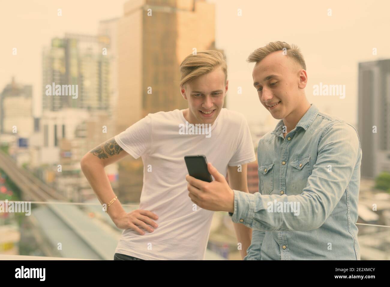 Deux jeunes hommes beaux avec des cheveux blonds ensemble contre la vue de la ville en noir et blanc Banque D'Images