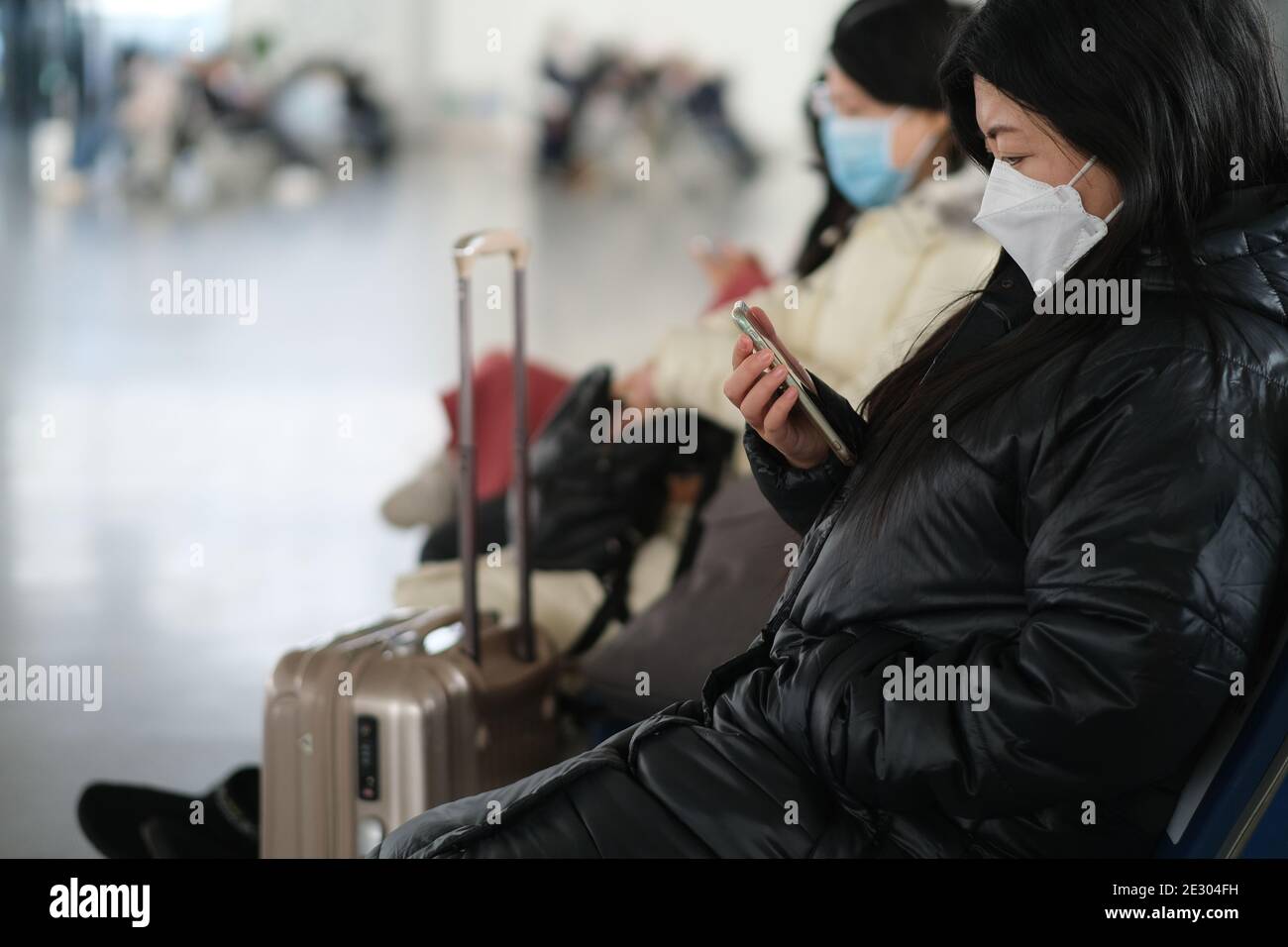 vue latérale d'une jeune femme dans un masque facial avec un téléphone et une valise. Concept de transport à la gare ou à l'aéroport Banque D'Images