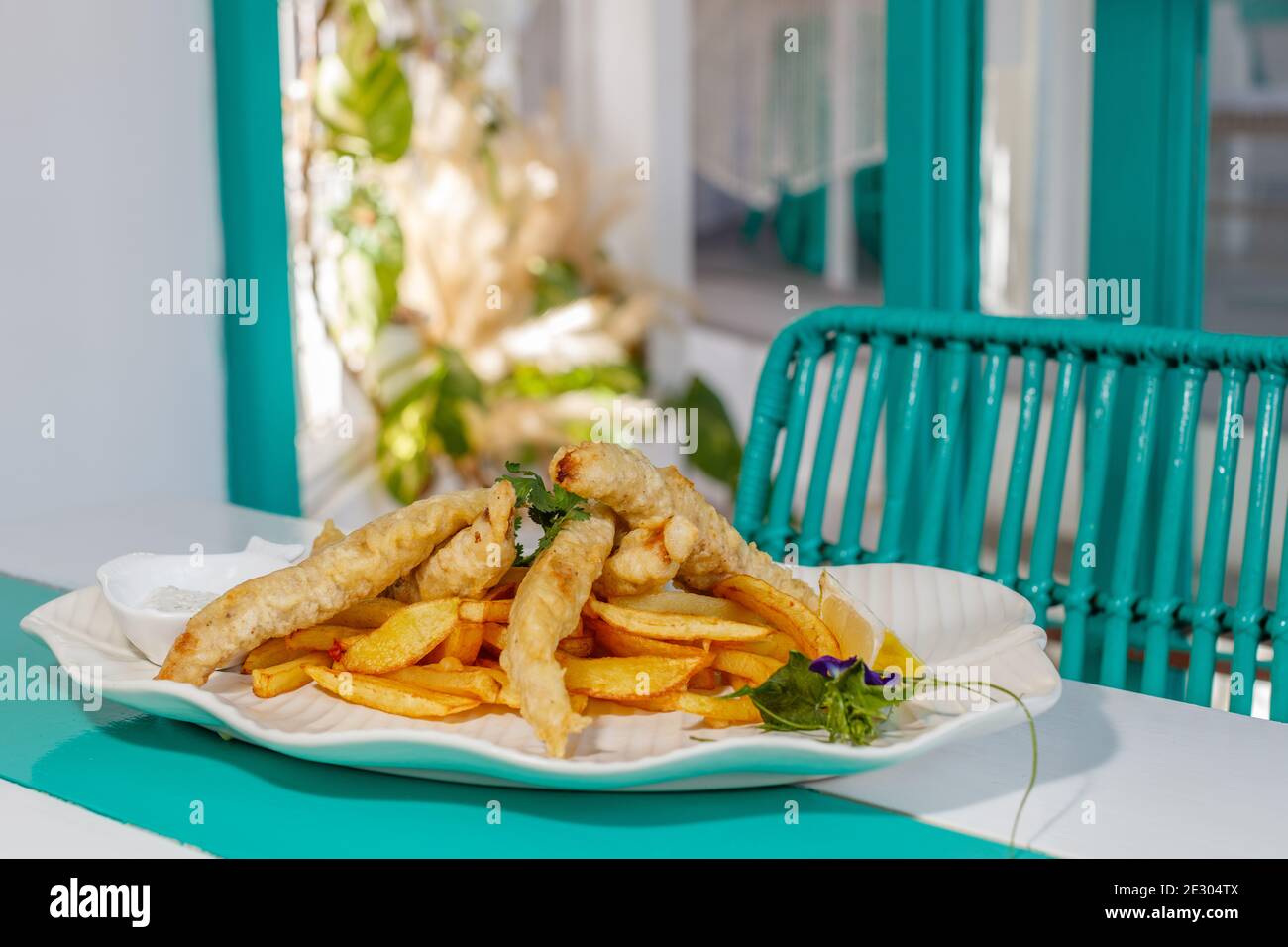 Poisson et frites avec sauce et citron, décoré de fleurs de pois papillons. Servi sur une plaque en céramique blanche. Banque D'Images
