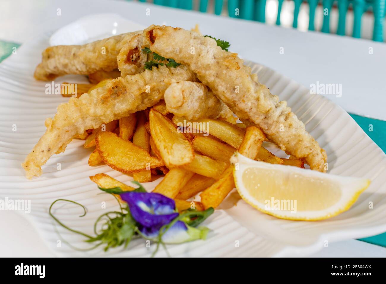 Poisson et frites avec sauce et citron, décoré de fleurs de pois papillons. Servi sur une plaque en céramique blanche. Banque D'Images