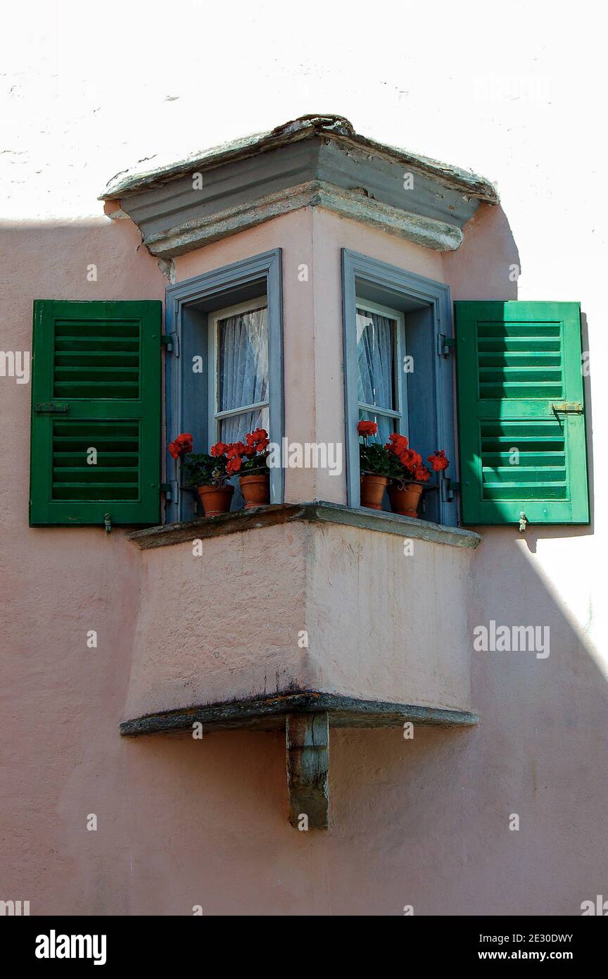 Petit balcon ancien avec fenêtres en bois et géraniums rouges dans la petite ville de Tirano, Alpes italiennes, Valtellina, province de Sondrio, Lombardie, Italie, UE. Banque D'Images