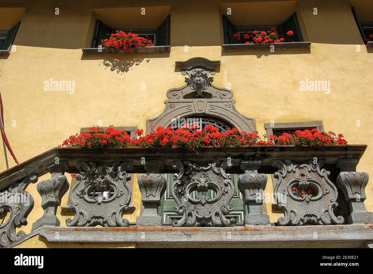 Ancienne maison avec balcon en pierre, porte et fenêtres avec géraniums rouges, ancien village de Zuoz, station touristique dans la vallée d'Engadin, Suisse. Banque D'Images