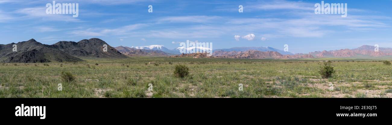 Panorama de la vallée de Bayan Olgi avec steppe d'herbe et quelques maisons et montagnes noires et grandes montagnes avec neige en arrière-plan. Banque D'Images